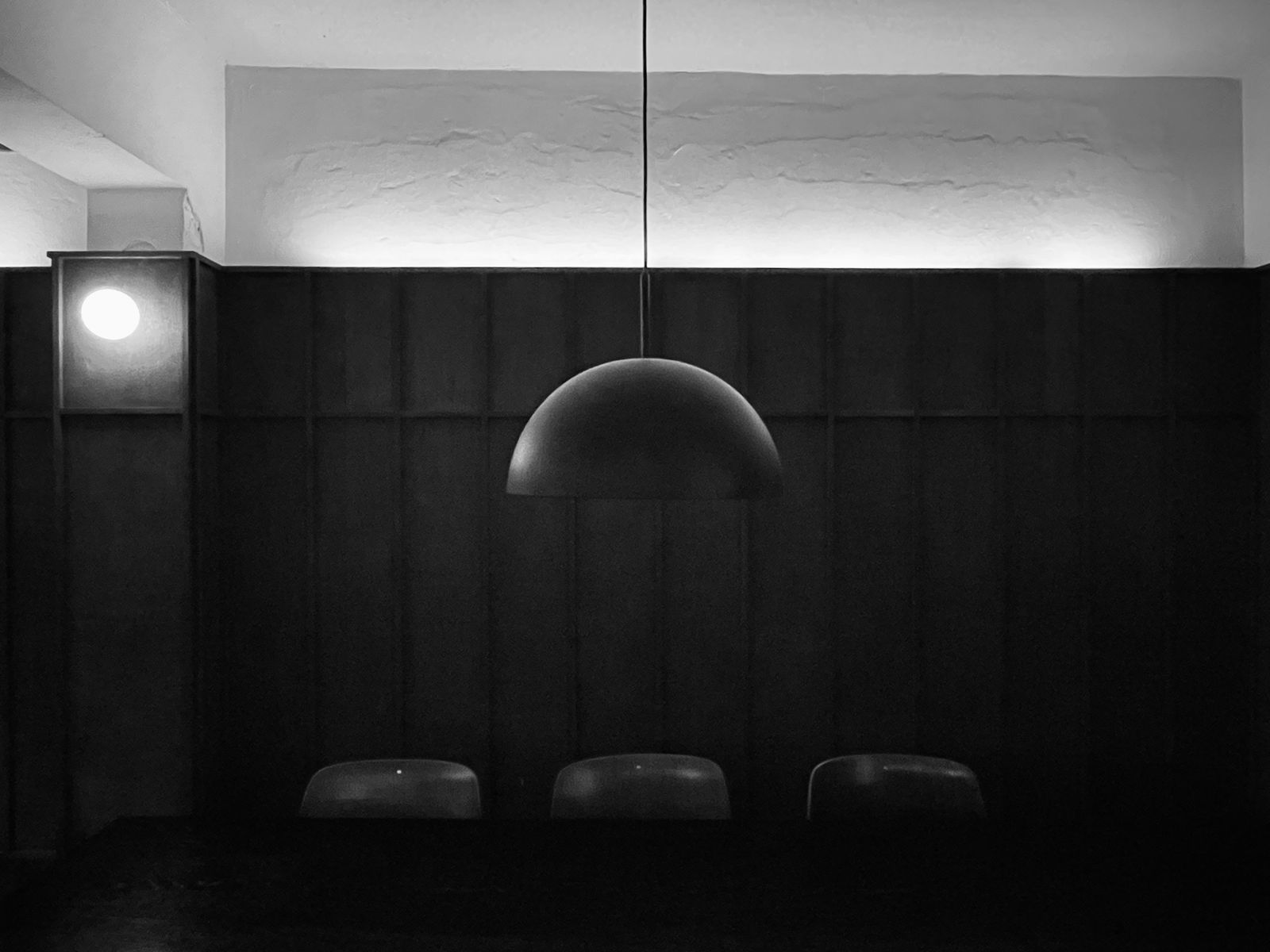Three chairs arranged beneath a large hemispherical pendant lamp