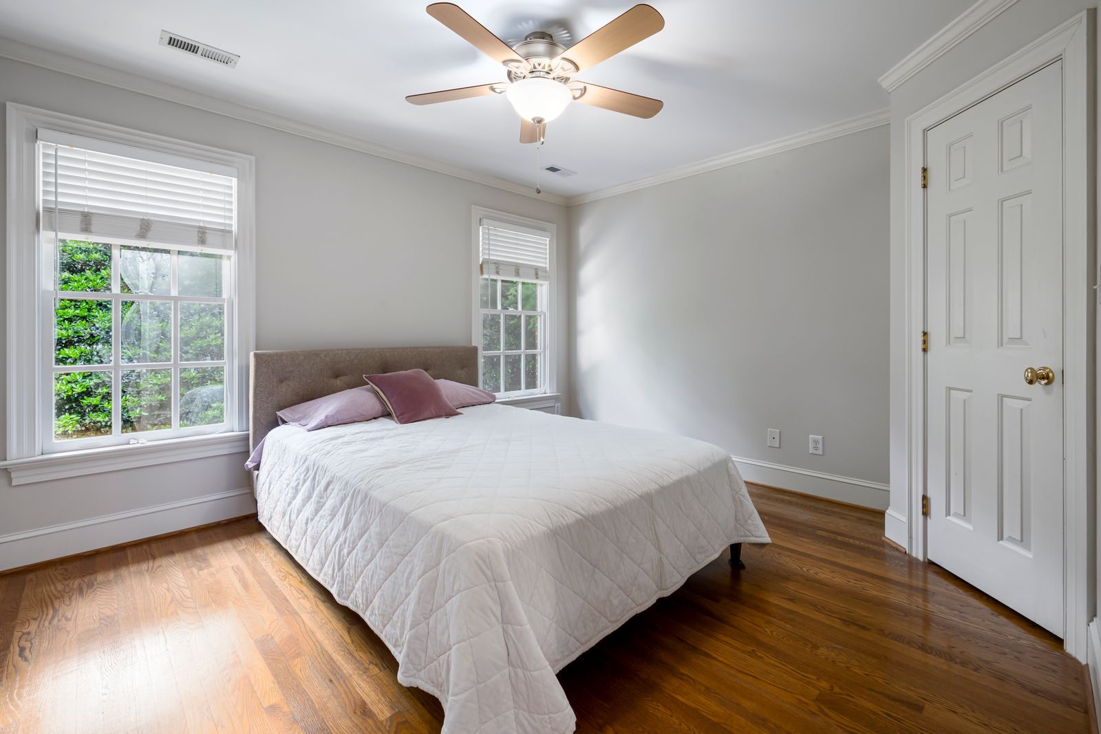 Bright bedroom with white bedding, a ceiling fan and large windows