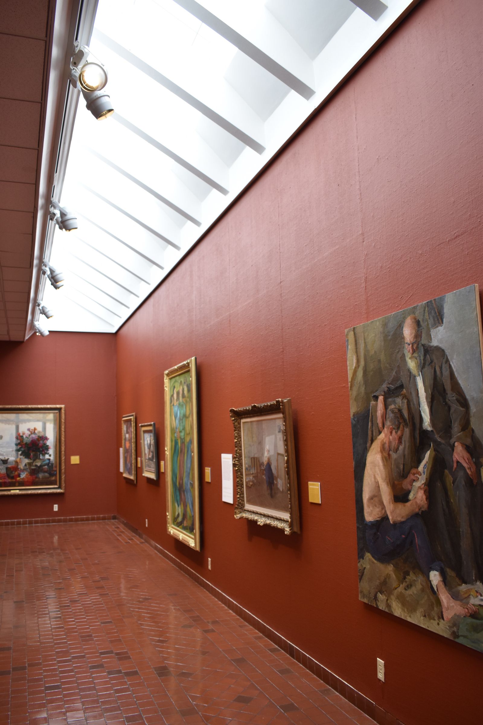 Gallery room hung with framed paintings above a polished floor
