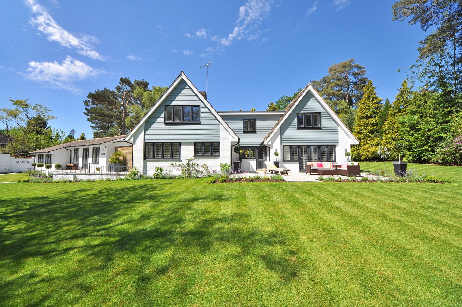 Two-storey white wooden house with a lawn and trees under blue sky